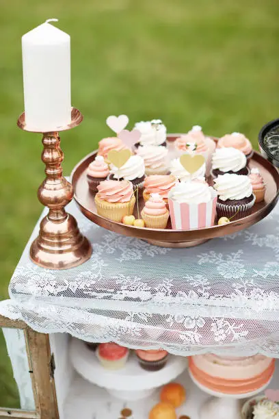 Cupcakes and a wedding cake on a sweet table closet outdoors on a meadow in shades of pink, white and gold