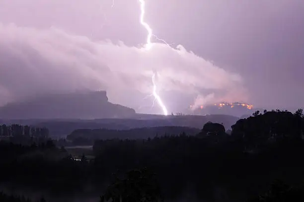 Thunderstorm in the Saxon Switzerland (German: Sächsische Schweiz, or Elbsandsteingebirge) near Dresden, overlooking the mountain Lilienstein (left side) and the illuminated fortress of the mountain Königstein.