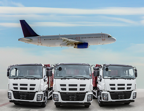 Three trucks are frontal front view and the plane is flying in the sky. Transportation concept.