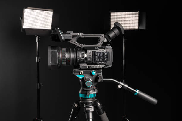 istock Side view of professional 4K video camera on camera tripod and two lighting LED panel on black background 1199165578