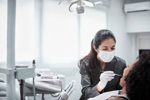 Female dentist examining patient in clinic Female dentist examining teeth of patient on chair. Young woman is visiting doctor for dental checkup. They are at clinic. dental hygienist stock pictures, royalty-free photos & images