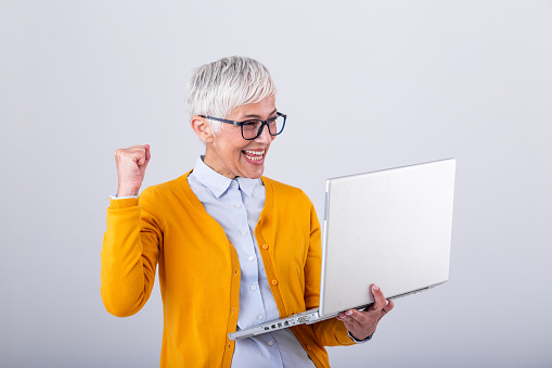 Happy mature middle aged elderly business woman winner excited by reading good news looking at laptop, glad senior older lady watching celebrating online bid bet win or great result victory concept