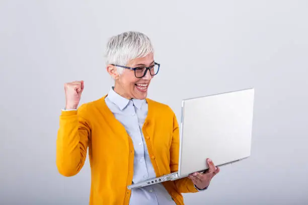 Photo of Happy mature middle aged elderly business woman winner excited by reading good news looking at laptop, glad senior older lady watching celebrating online bid bet win or great result victory concept