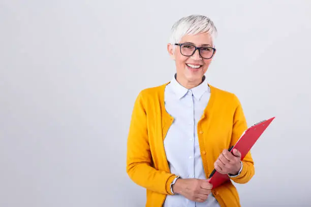 Photo of Mature business woman holding document on clipboard and glasses isolated on white background. Serious business woman looking at documents while holding her glasses in other hand