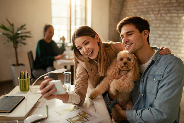 istock Young colleagues having fun while taking selfie with a poodle in the office. 1199168643