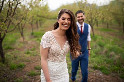 Bride and groom holding hands and walking down an orchard.