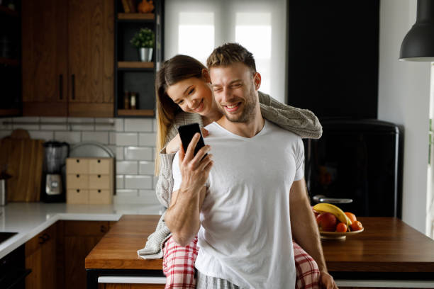 istock Young affectionate couple looking at mobile phone in the kitchen 1199175878