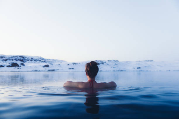 mujer que se baña en la piscina termal con vistas a las montañas nevadas y lago congelado en islandia - baños térmicos fotografías e imágenes de stock