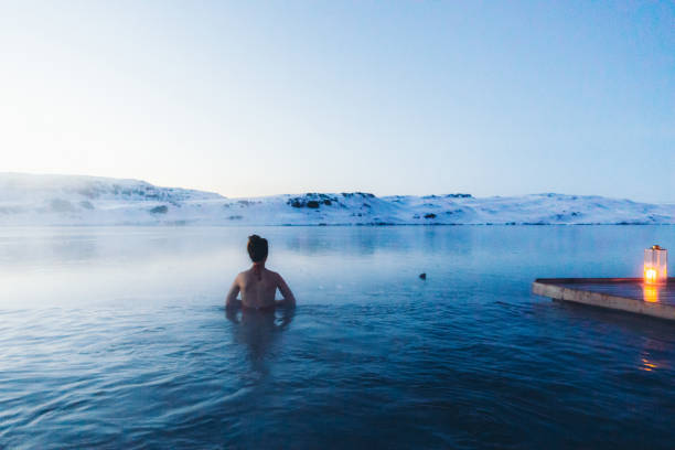 mujer que se baña en la piscina termal con vistas a las montañas nevadas y lago congelado en islandia - baños térmicos fotografías e imágenes de stock