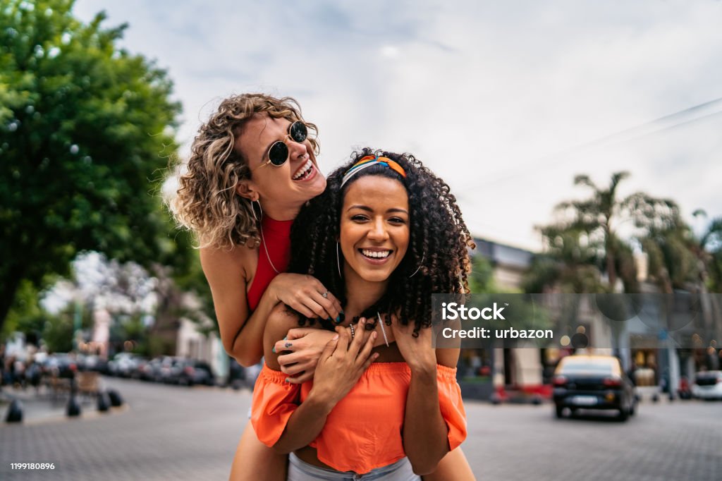 Two beautiful women having fun Two young beautiful smiling Argentinian women having fun at city street, having a piggyback ride. Shooting Buenos Aires, Argentina. Friendship Stock Photo