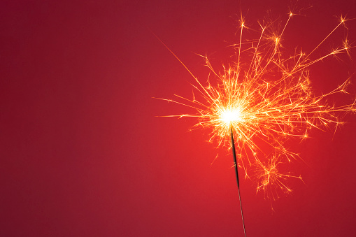 Christmas or Happy New Year party concept. Close up of Bright burning sparkler on a red background. Copy space.
