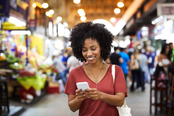 Smiling woman using smart phone at supermarket Smiling woman text messaging on smart phone. Happy female customer with curly hair is wearing casuals. She is shopping at supermarket. Happy Customer stock pictures, royalty-free photos & images