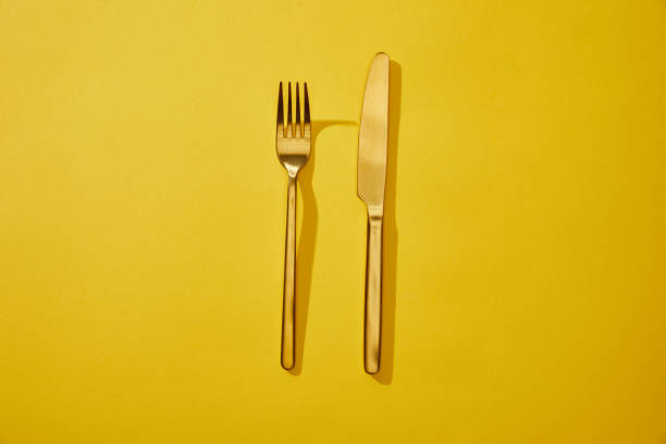 istock Top view of shiny fork and knife on yellow background with copy space 1199186588