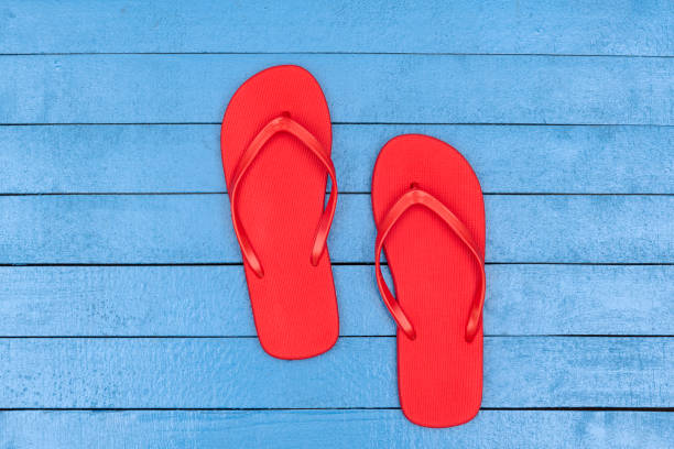 Red flip flops in the black sand and silhouette of woman in red swimsuit standing on the ocean beach. Summer concept.