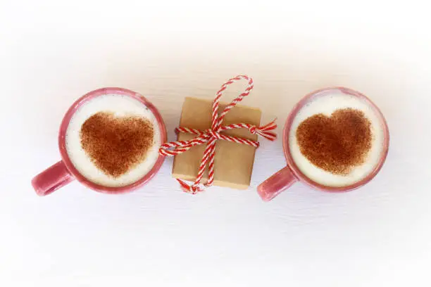 gift between two cups with foamy cappuccino decorated with cocoa hearts