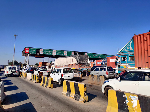 Jaipur, Rajasthan, CIRCA 2020 - Toll booth gates occupied by different types of vehicles such as cars, trucks, personal vehicles, commercial vehicles, to pass through. The top of the booth shows the lanes that accept fastag system for easy pass