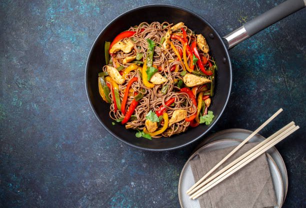 fideos soba de trigo sarraceno plato japonés con pollo y verduras de zanahoria, pimiento y judías verdes en wok sobre fondo azul oscuro - wok fotografías e imágenes de stock