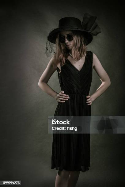 Studio Portraitgirl Black Dress Hat And Sunglasses Stands On A Dark Background Stock Photo - Download Image Now