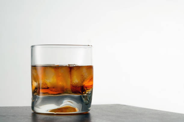 テーブルの上に氷の立方体と熟成した金色のウイスキーのグラス。バーで岩とアンバー色のアルコール飲料 - whisky liqueur glass alcohol bottle ストックフォトと画像