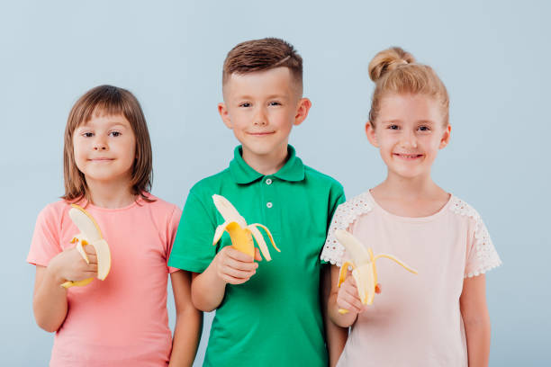 istock caucasian three kids with bananas in hand. isolated on blue background, copy space, in studio 1199197776