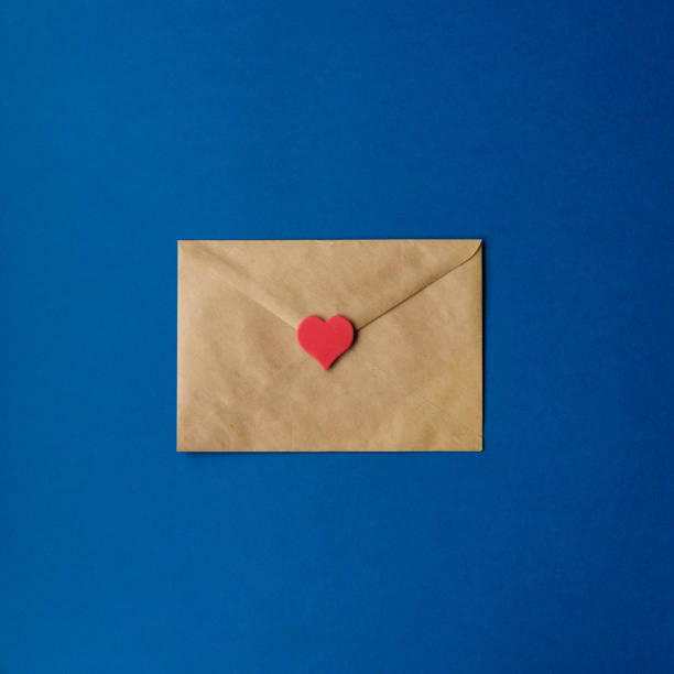 st. valentin s umschlag von handwerk papier mit rotem herzen auf klassischen blauen hintergrund mit kopierraum. farbe 2020. top-ansicht, quadratische ernte. - liebesbrief stock-fotos und bilder