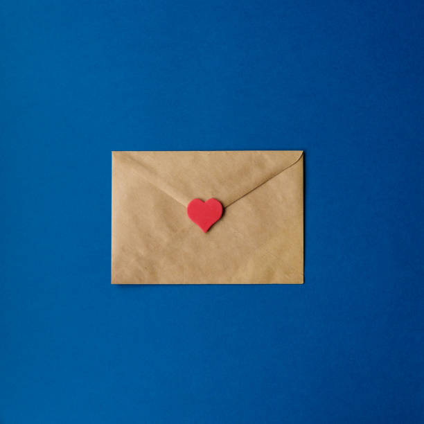 コピースペースを持つ古典的な青い背景に赤い心を持つクラフトペーパーの聖バレンタインの封筒。カラー 2020.上図、正方形のトリミング。 - love letter ストックフォトと画像