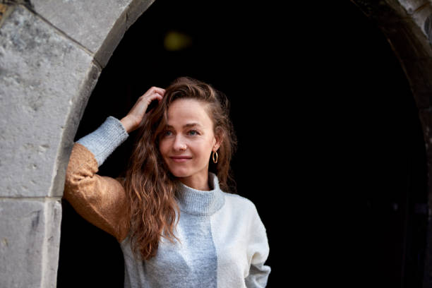 Cropped shot of a cheerful young woman leaning against a doorway outside during the day