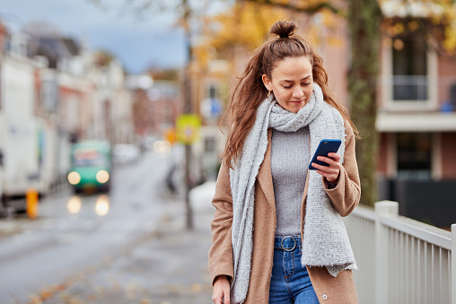 Cropped shot of a carefree young woman texting on her cellphone while waking on a sidewalk in a busy city outside during the day