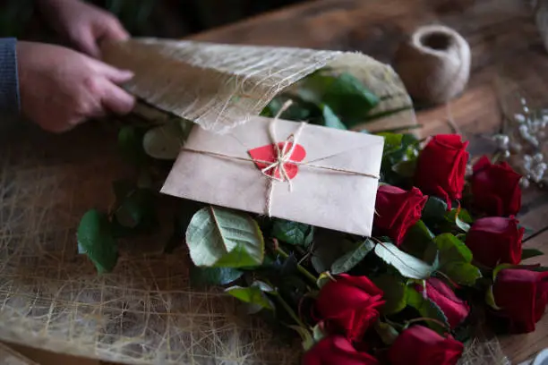 Unrecognizable woman florist arrange flowers, woman's hands creating a bouquet of rose flowers on a wooden table.