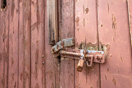 Rotting wooden garage door with broken lock painted in pink.