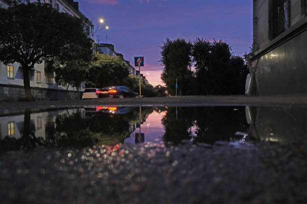 Low shot of puddle whilst it rains with city traffic