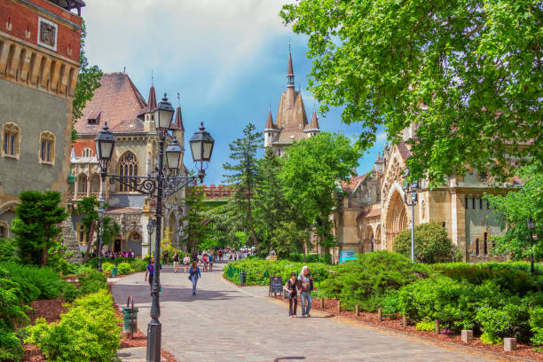 Budapest/Hungary- May 8, 2018: spring cityscape with Vajdahunyad Castle complex courtyard, featuring copies of several landmark buildings from different parts the Kingdom Hungary, beautiful park and walking tourists.