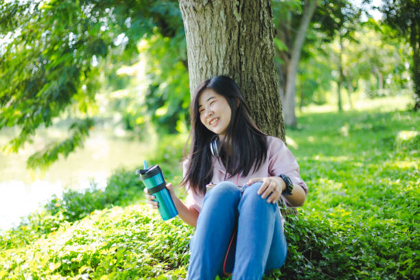 istock Asian woman drinking coffee while sitting in the park 1199229257