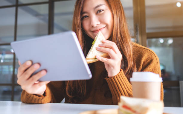 istock woman holding and eating whole wheat sandwich while using tablet pc 1199230318