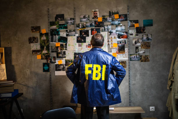 FBI detective looking at wall full of evidences and crime scene pictures Rear view of FBI detective wearing FBI raincoat and looking at wall full of evidences and crime scene pictures with hands on hip fbi photos stock pictures, royalty-free photos & images