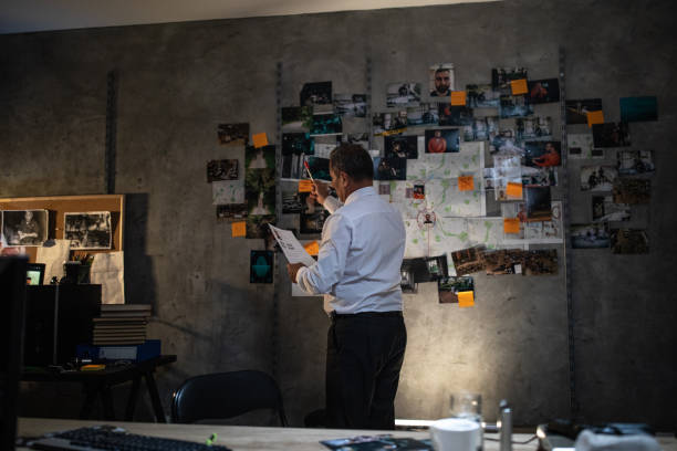detective della polizia che guarda il giornale davanti al muro con mappa e immagini in ufficio - evidence marker foto e immagini stock