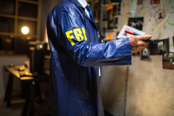 detective dell'fbi che guarda la foto della scena del crimine mentre si trova di fronte al muro - evidence marker foto e immagini stock