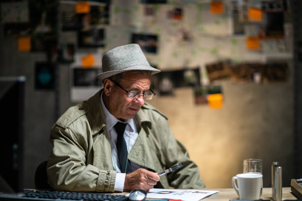istock Mature detective looking sitting at the desk and using magnifying glass 1199232027