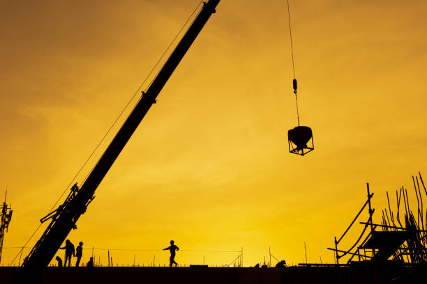 istock Silhouette construction working and machinery crane hoisting cement mortar mixer bucket container in construction site 1199234200
