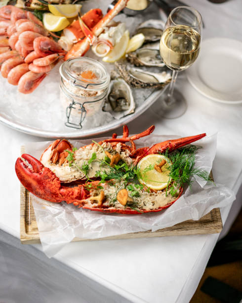 Baked lobster on a white table Baked, gratinated lobster with garlic butter, lemon, chantarelles and parsley. Served on a wood board. Champagne flute lobster seafood photos stock pictures, royalty-free photos & images