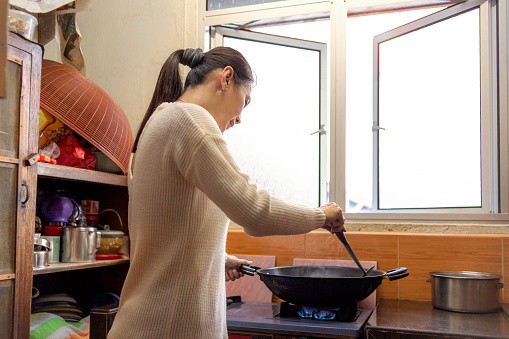 Asian woman making lunch for the family, cooking in apartment kitchen using wok