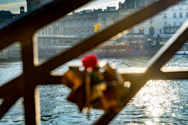 2019 The River Seine in Paris with the Passerelle des Arts bridge in the background viewed throughout of focus mementoes on a wrought iron fence in winter. Paris, France.