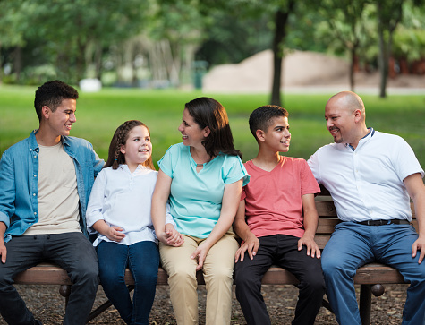 Happy latin parents sitting on a bench with their kids and smiling at them.