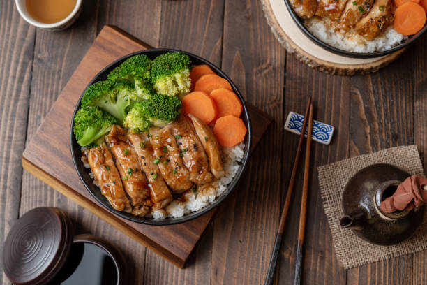 japanese food style : top view of homemade chicken teriyaki grilled with rice , carrot , broccoli put on the black bowl and place on wooden table - teriyaki broccoli carrot chicken imagens e fotografias de stock