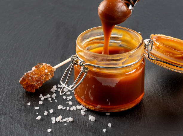 istock Spoon with tasty caramel sauce over jar on table. 1199249577