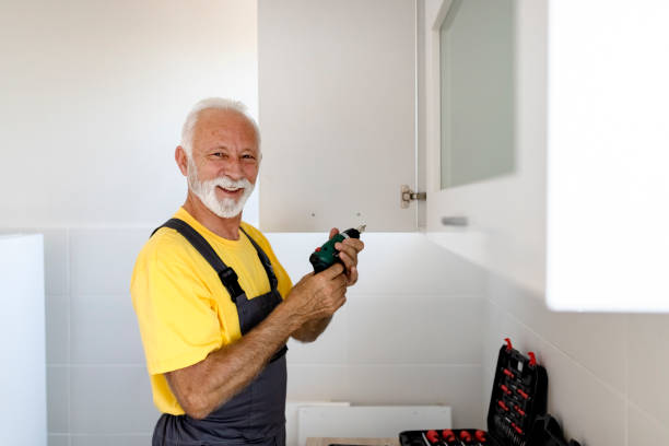 Elderly Handyman With an Electric Drill in His Hands Assembles the Kitchen Looking at Camera