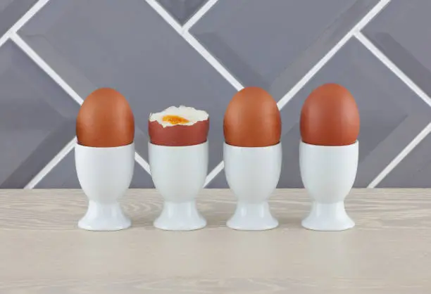 Four eggs in eggcups on wooden kitchen surface