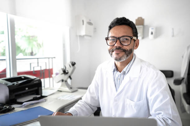porträt eines reifen männlichen arzt es mit laptop im krankenhaus - doctor male doctor mature men portrait stock-fotos und bilder