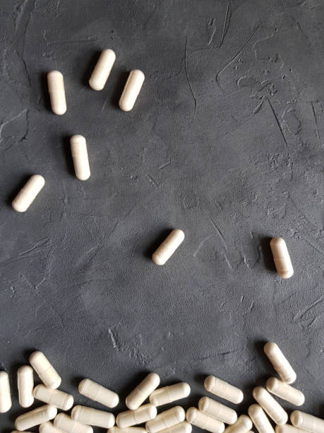 white gel capsules medical preparation on a gray concrete background. the concept of classical medicine and treatment, healthy lifestyle, dietary supplements, naturopathy and alternative medicine. vertical photo - perscription capsule frame pill imagens e fotografias de stock