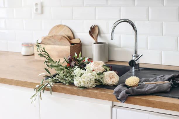 Closeup of kitchen interior. White brick wall, metro tiles, wooden countertops with kitchen utensils. Roses flowers in black sink. Modern scandinavian design, home staging, cleaning concept. primer plano del interior de la cocina. muro de ladrillo blanco, azulejos de metro, encimeras de madera con utensilios de cocina. flores de rosas en fregadero negro. diseño escandinavo moderno. puesta en escena en el hogar, concepto de limpieza.